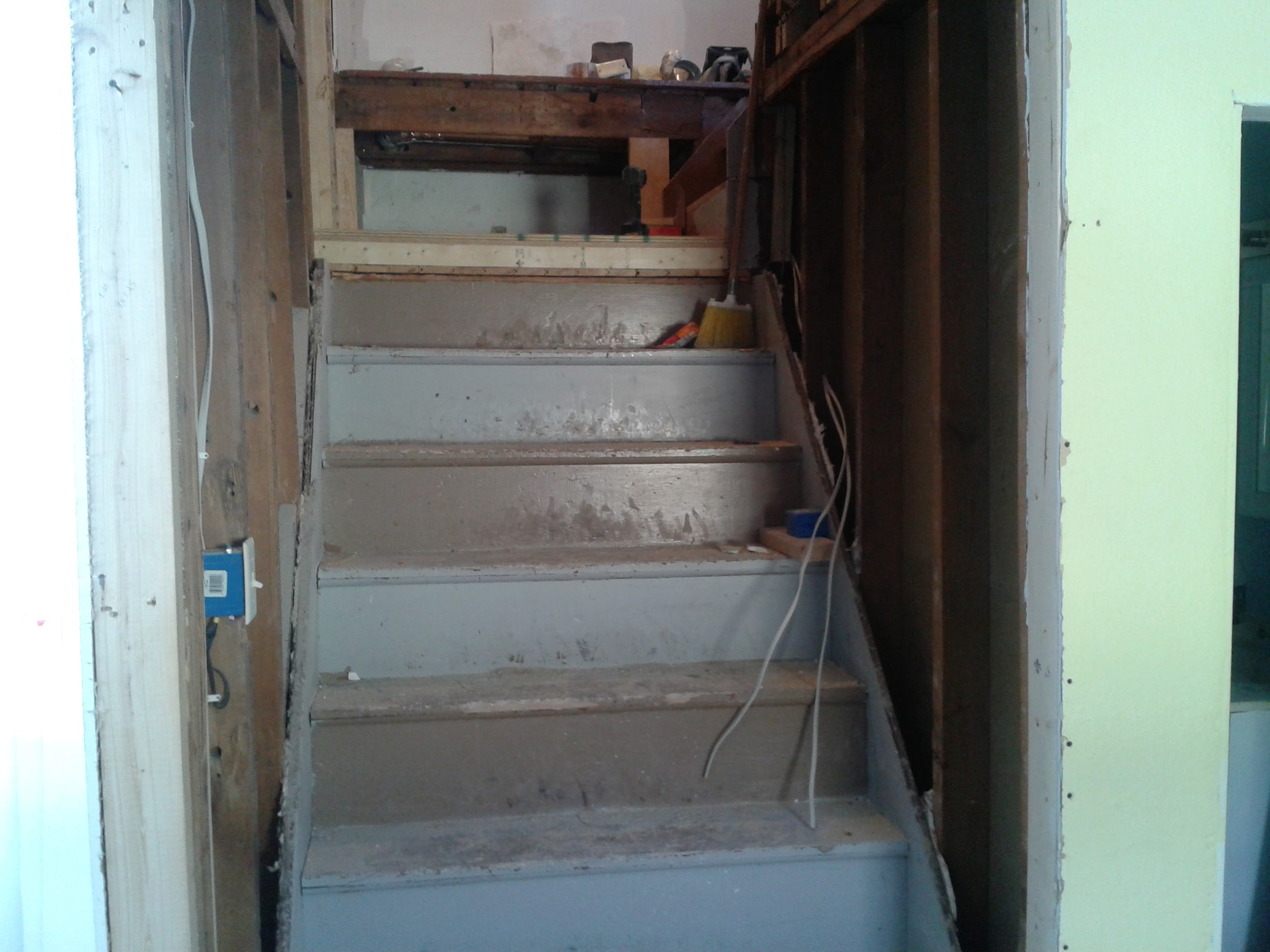Original staircase with old painted treads and exposed framing during demo