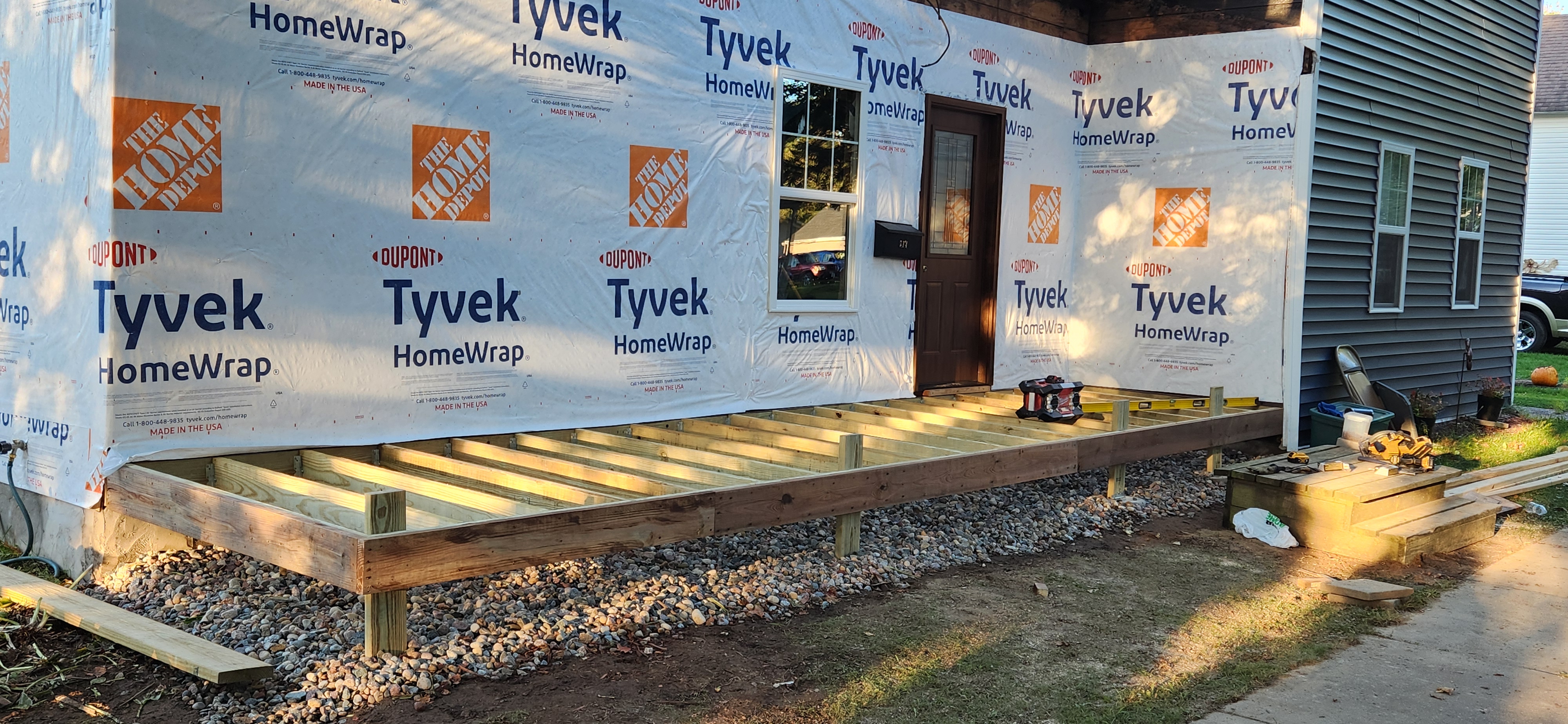 Porch deck framing with pressure-treated joists and Tyvek wrap on exterior