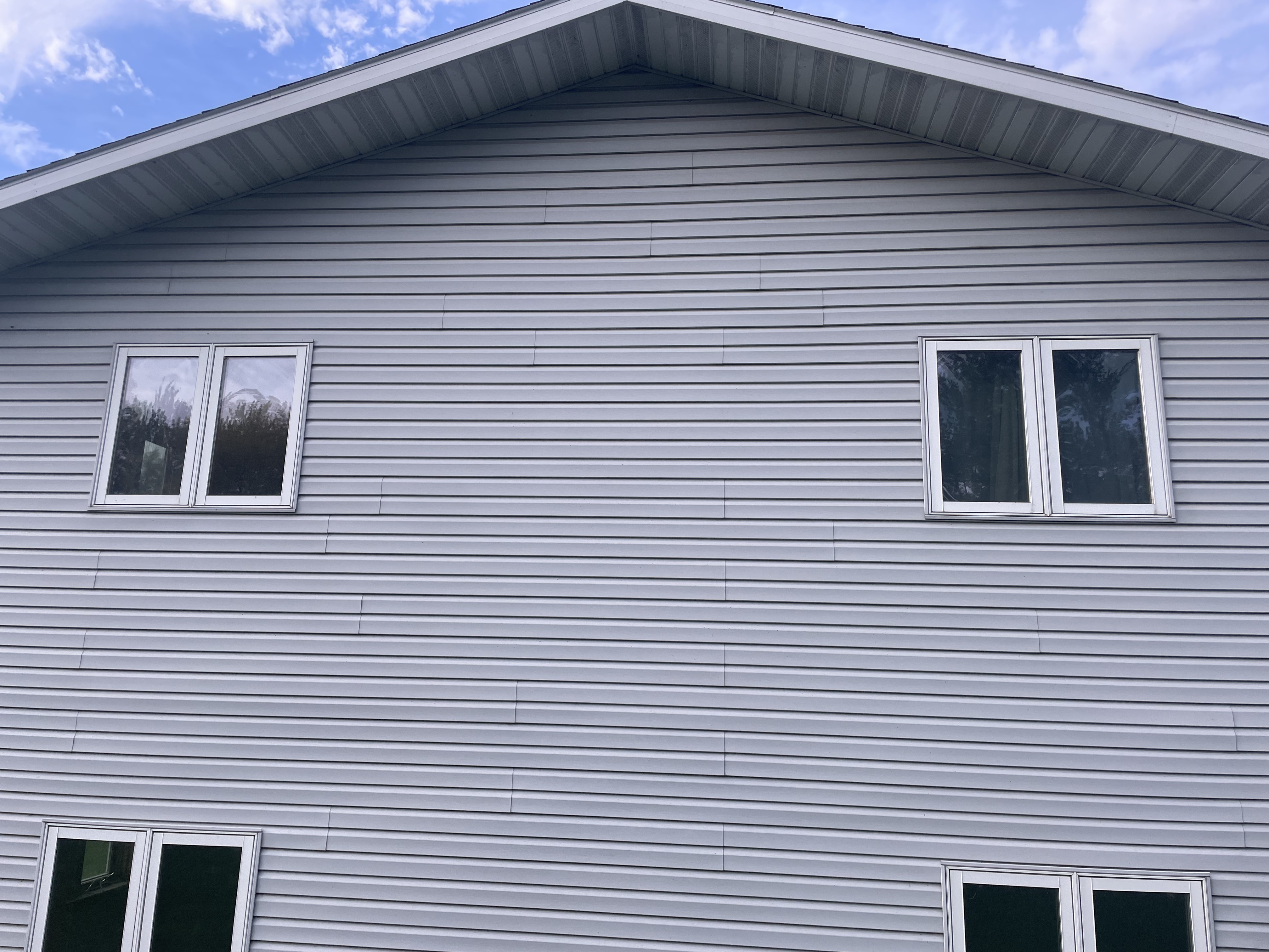 Completed exterior with new gray vinyl siding and white windows installed